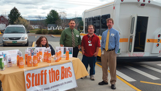 Photo of four people in front of a bus at a table advertising a stuff the bus event